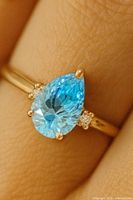 Ring on finger view, showing pear-cut blue stone and gold band