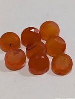 Eight round faceted orange carnelian stones on white surface