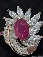 Top view of silver ring with oval ruby stone surrounded by marquise and baguette CZs