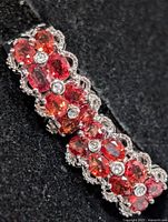 Close-up of one earring showing orange sapphires and clear accents