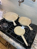 Three cream enamel cast iron frying pans on stovetop