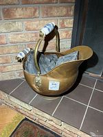 Front view of copper coal scuttle showing ceramic handle grip, interior contents, and brick fireplace background