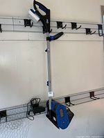 Full view of Snow Joe cordless snow shovel hanging on wall with battery installed and charger visible