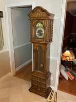 Full view of wooden grandfather clock with pendulum and two brass weights on floor