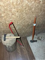 All three tools grouped: bow saw, hatchet style maul on log, full-size maul standing