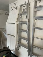 Full view of folded aluminum step ladder hanging on wall