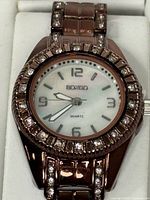 Close view of watch dial, bezel with crystals, brown link band