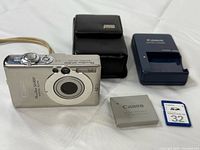 Front view of Canon PowerShot SD300 camera with battery, charger, case and SD card displayed