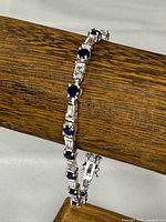 Full view of bracelet wrapped around wood dowel, showing alternating blue round and clear baguette stones