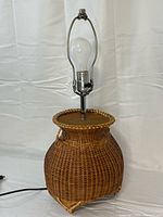 Full view of wicker table lamp with bulb, harp and cord