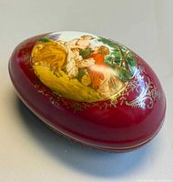 Closed egg-shaped burgundy porcelain trinket box showing courting scene and gilt decoration