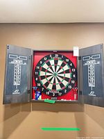 Cabinet open showing dartboard, scoreboards, darts and chalk