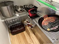 Overall shelf view showing stock pot, saucepan, Paderno pan, wok pan, roasting pan, fondue box, egg-poacher pan