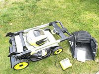 Mower folded with grass bag, charger and manual on grass