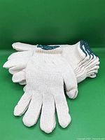 Stack of off-white cotton knit gloves showing green cuff trim