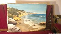 Full view of unframed seascape painting on red couch