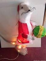 Full view of tinsel otter figure with coat, ornament and lights