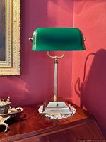 Front view showing entire lamp on table, green glass shade, brass column and base