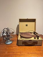 Overall view of Victrola record player open with Torcan desk fan beside it on wooden surface
