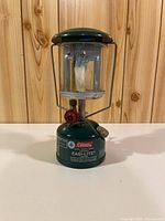 Front view showing Coleman label, globe, mantle, red control knob