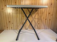 Side view of assembled gray plastic folding table showing X-frame legs