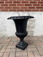 Front view of black cast iron urn planter on brick patio