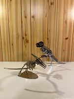 Both metal dinosaur skeleton figurines on white surface against wood backdrop