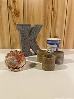 Group shot of all items: letter K, cup, seashell, three stone candle holders