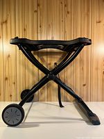 Side view of folded-out stand showing X-frame legs, wheels, and plastic top.