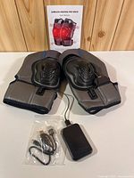 Both knee wraps, battery pack, USB cable and manual displayed