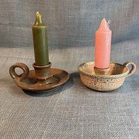 Front view of two pottery chambersticks with candles inserted