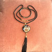 Full view of pendant necklace with tassel and matching bangle on pink background