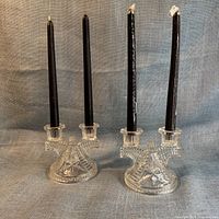 Two glass double-arm candle holders standing with four black taper candles inserted