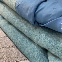 Close-up of folded teal wool blanket showing texture and satin edge