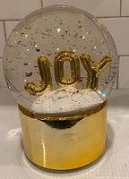 Overall view of snow globe showing JOY letters and gold base