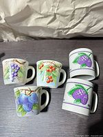 Five ceramic espresso mugs with various fruit designs displayed rim-up on tabletop
