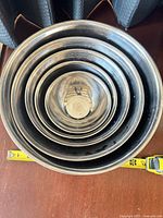 Five stainless steel bowls stacked showing nested fit with tape measure indicating largest diameter