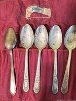 Five tarnished sterling teaspoons in red fabric roll