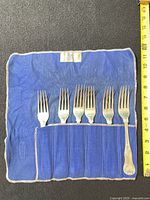 Six forks in blue roll beside measuring tape showing 8-inch length