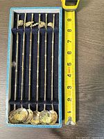 Top view of six straw spoons in box with tape measure showing length