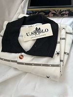 Folded polo shirt showing U.S. Polo Assn. hangtag and black collar