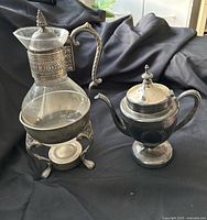 Front view of glass carafe on warmer and silver-plated teapot