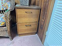 Front view of wooden 2-drawer file cabinet beside wicker chair