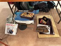 Overall lot showing electric skillet box, egg poacher set, fry pan, glass lid, cutting board, serving tray