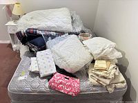 Pile of bedding showing comforters, sheets, pillows, fabric basket