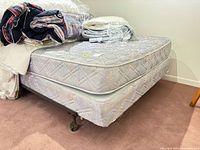 Mattress stacked on box spring atop metal frame with casters; bedding items visible on top