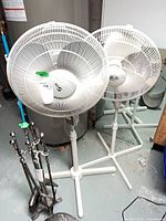 Two white pedestal fans standing side by side