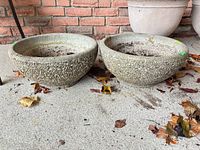 Two concrete bowl planters side by side on ground