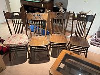 Front view of four spindle-back dining chairs showing carved crest rails, seat surfaces and cushion on one chair
