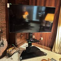 Front view of Sharp 65" TV on floor stand with remotes on shelf